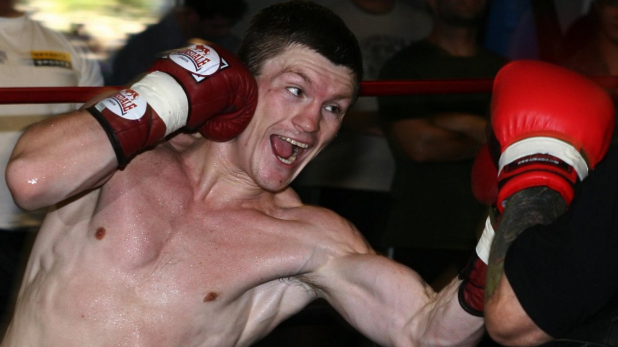 Ricky Hatton in the ring sparring with someone. He is wearing red gloves and the opponent is also wearing red gloves. Hatton has short dark hair and looks to be enjoying himself.