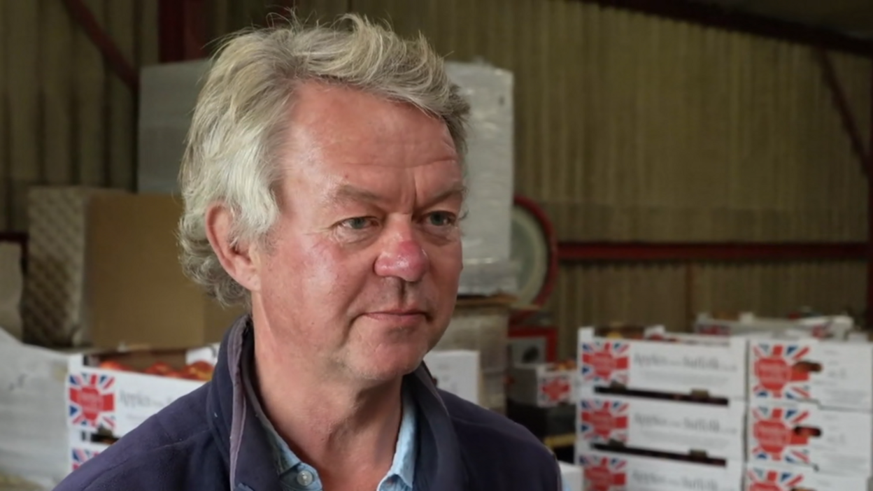 A head shot of Henry Dobell. He is looking past the camera. Boxes of apples are in the background. 