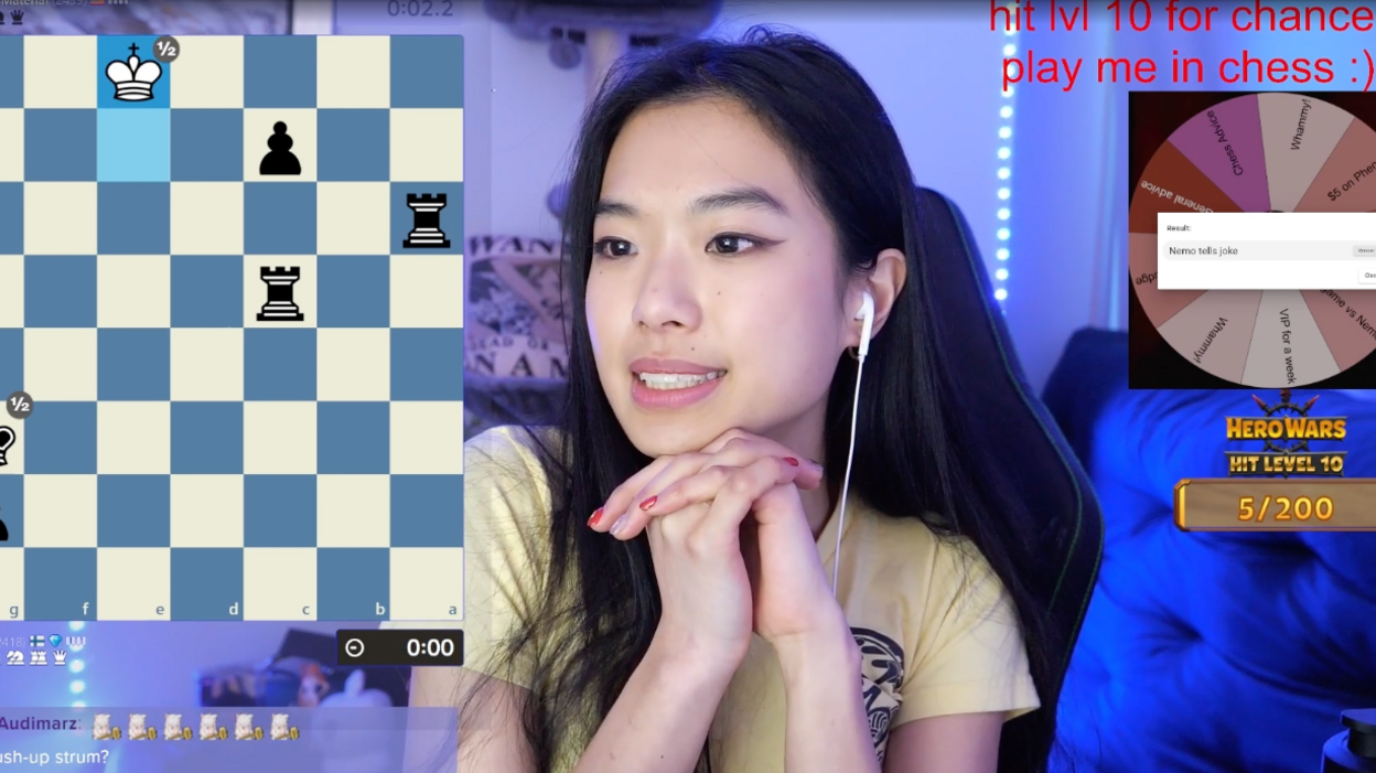 Screen shot of Nemo playing chess on Twitch. She is in the centre of the image, a chess board is visible on her left. On the right is a wheel of fortune and letters saying 'hit lvl 10 for chance play me in chess :)'. Her background is blue because of neon lightning. 