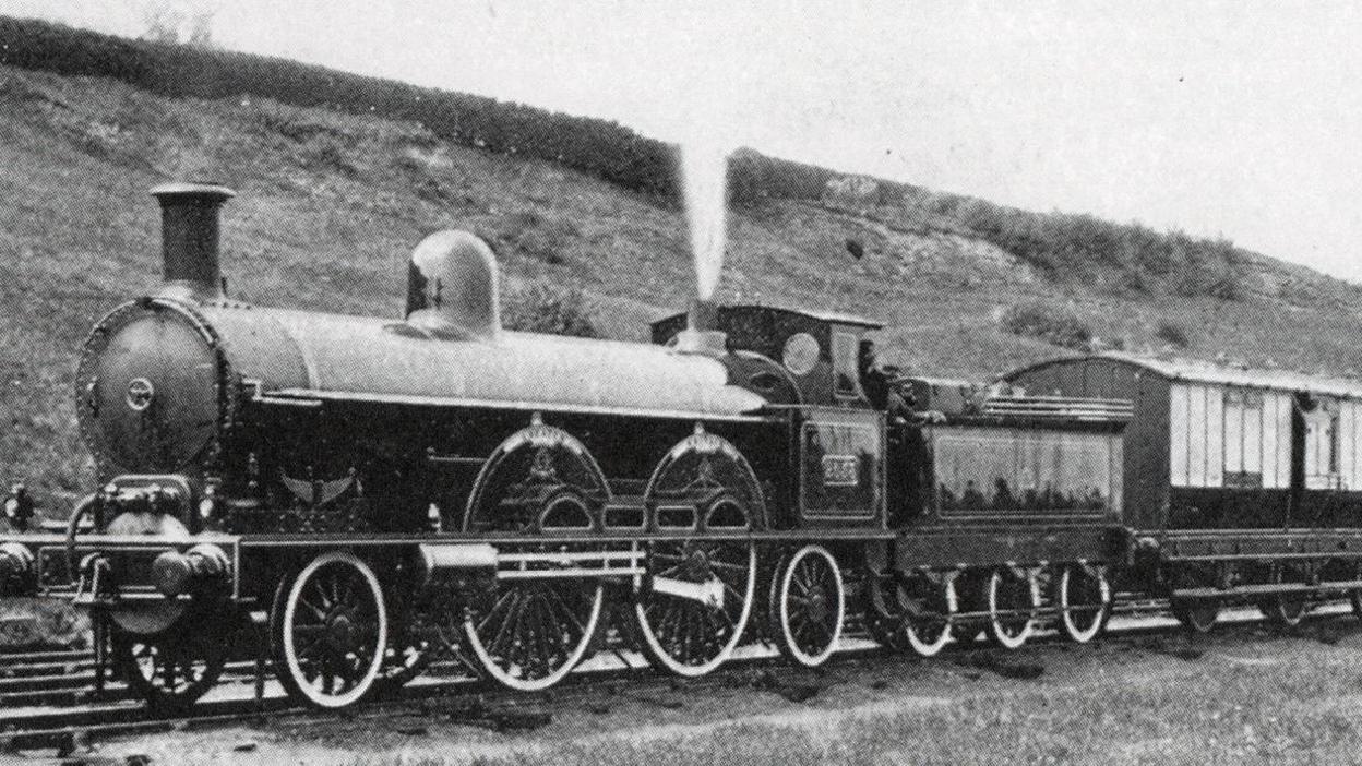 A black and white photo shows a steam locomotive pulling along the carts of the royal train.