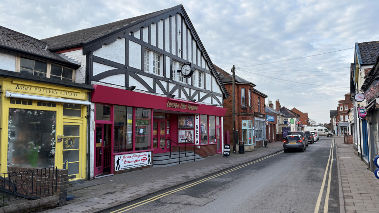 Leiston High Street. There is a yellow pottery studio, next to the cinema which has a burgundy coloured front and glass windows with steps leading up to the entrance. 