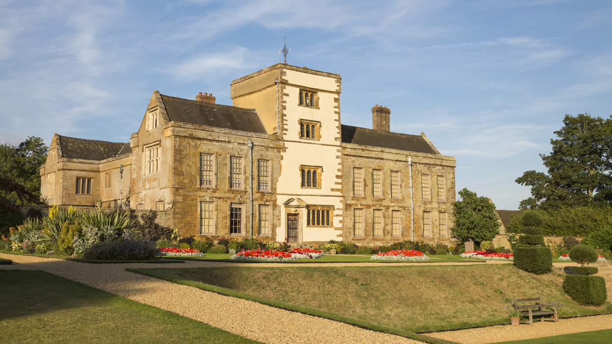 The frontage of a three-storey stately home, Canons Ashby, in the midst of lots of shrubs and plants