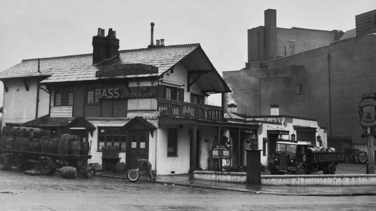 Black and white photo of Ye Olde Swiss Cottage pub in 1948 with a man rolling a barrel in the front