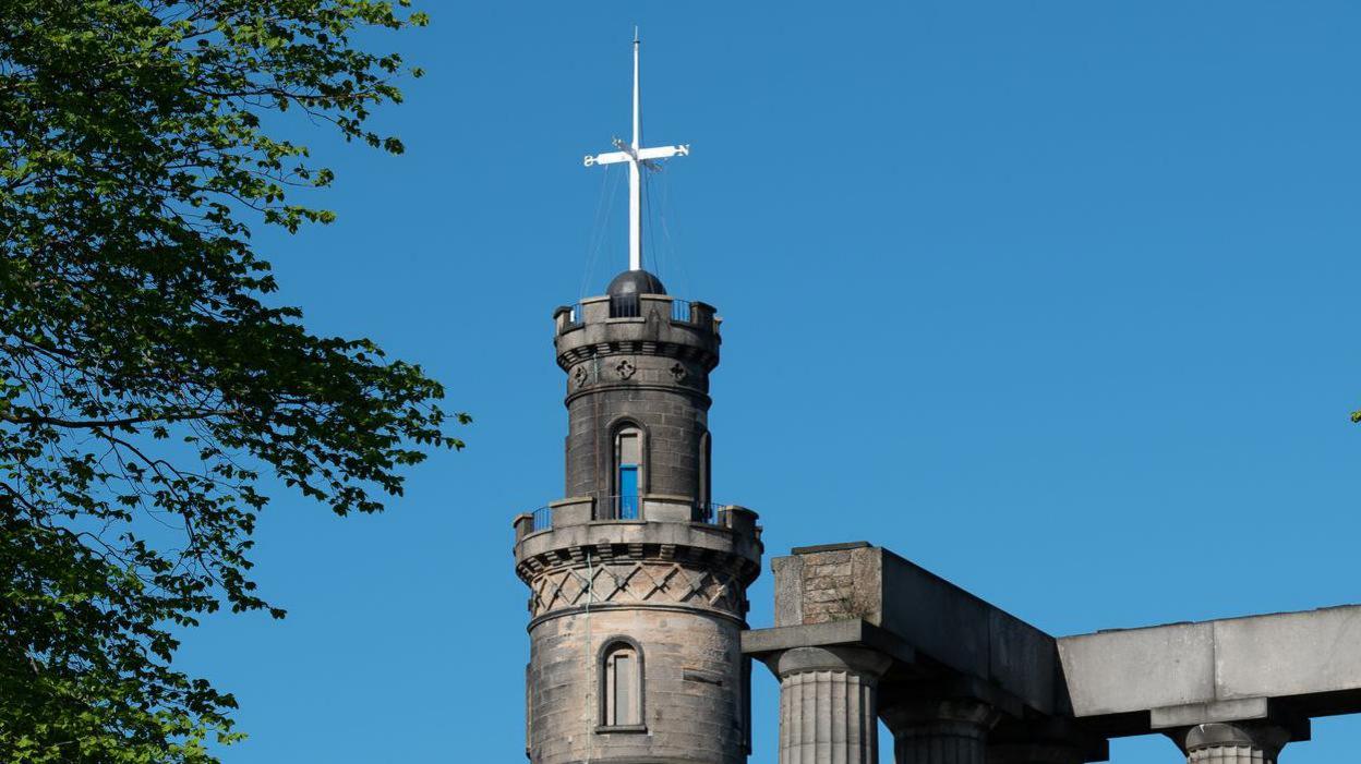 The ball is black in colour and at the bottom of a white pole-like structure which has arms pointing north, south, east and west. The contraption is on top of a round stone-built turret-like structure.