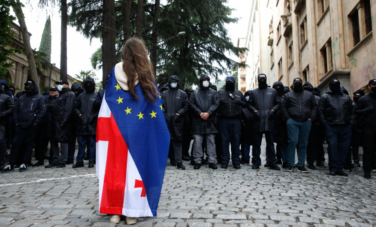 A protester wearing a Georgian and European flag faces off policemen blocking a street during a rally against a draft bill on 'foreign agents' near the Parliament building in Tbilisi, Georgia