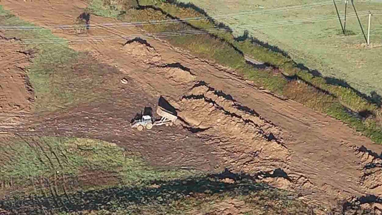 An aerial shot of a tractor and trailer filling trenches with waste 