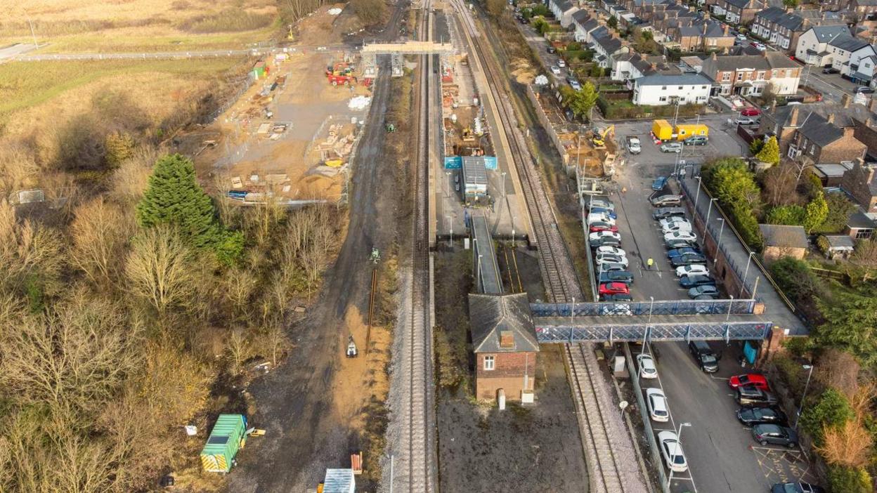 An aerial view of Eaglescliffe station. The existing footbridge can be seen leading from the car park to the station. To the left, a building site can be seen.