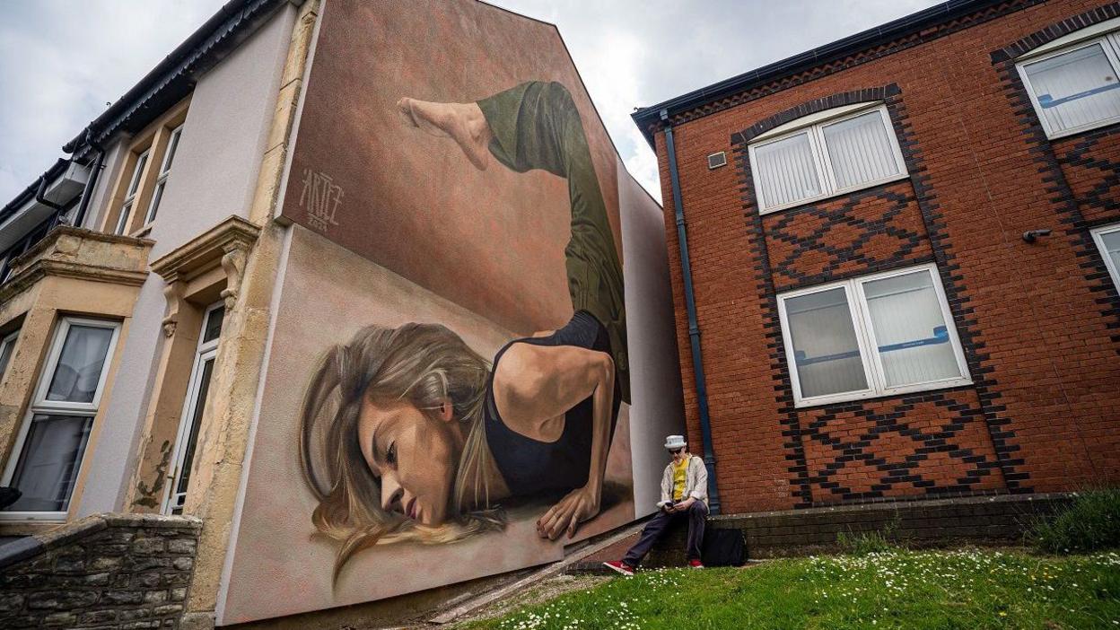 A huge mural of a woman performing a handstand on the side of a house in Bristol as part of Upfest Presenta