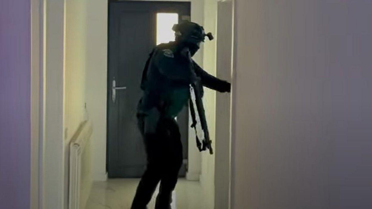 A screengrab from a video shows an armed police officer searching a house