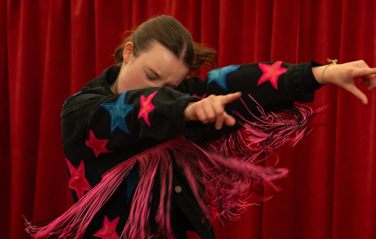 Bella Ramsey wearing a black jumper with stars on pointing while dancing