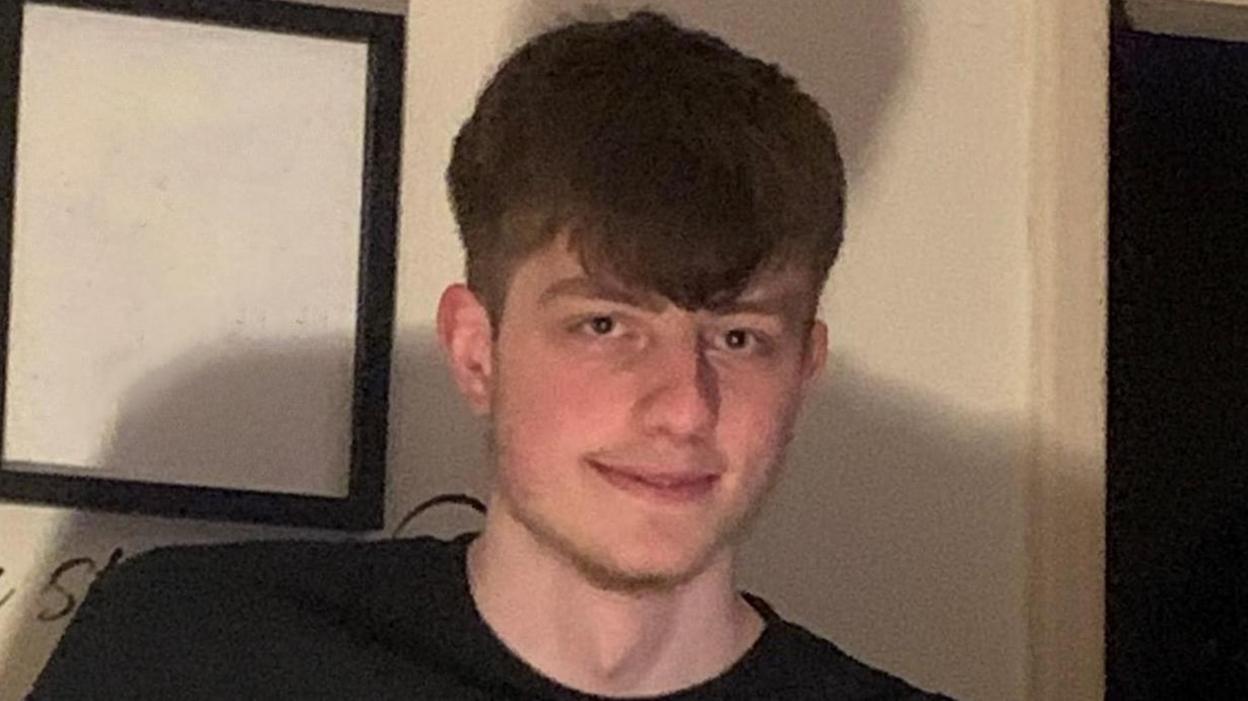 David Eubank, smiling and with brown hair, wears a dark t-shirt as he poses for a photograph in front of white wall.