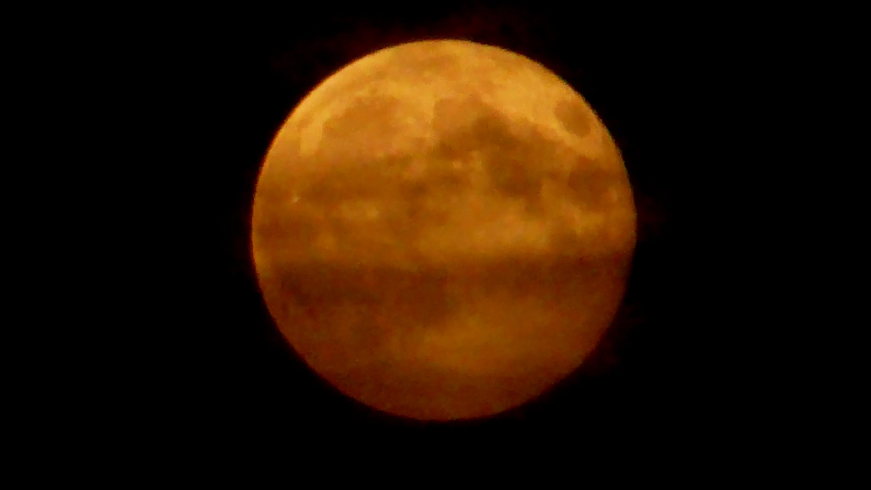 The image shows a close-up of the full moon with a striking orange hue.