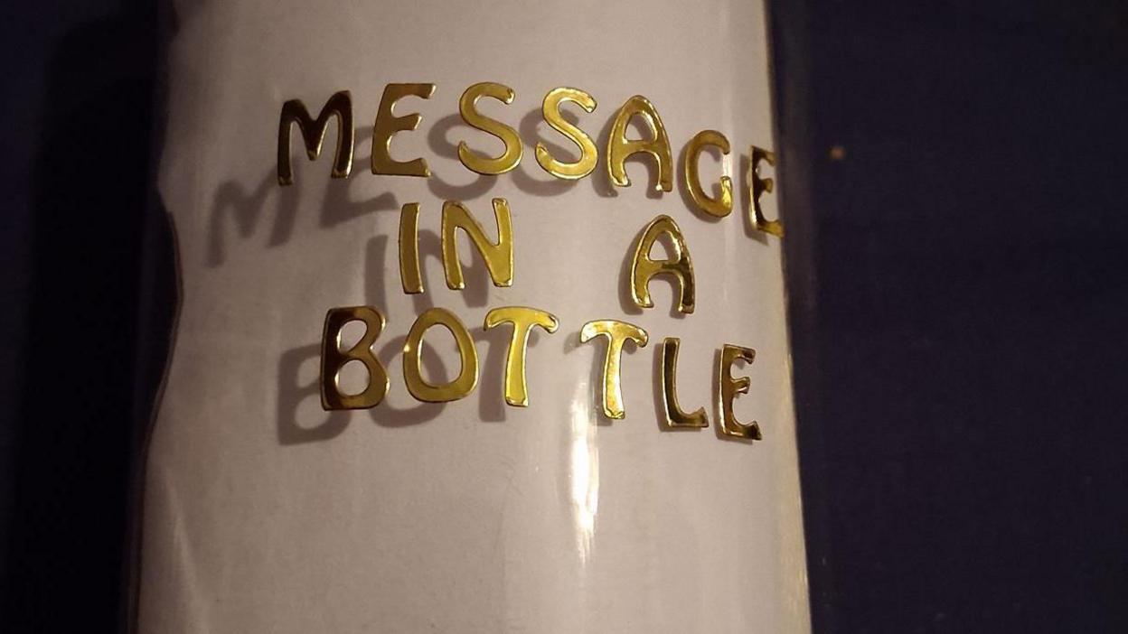 Close up of bottle with the words Message in a Bottle written on it in gold letters