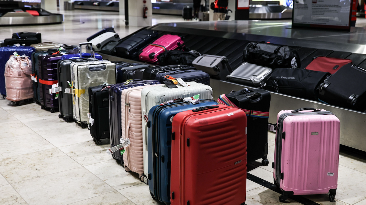 A stock image of dozens of suitcases lined up alongside a luggage carousel. There are more bags on the carousel itself.