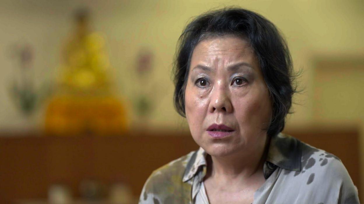 Portrait of Mungnee, a middle aged Chinese Malaysian woman being interviewed in front of a Buddha statue