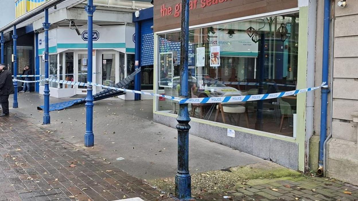 A row of shops is cordoned off, with metal shutters which have been smashed off.