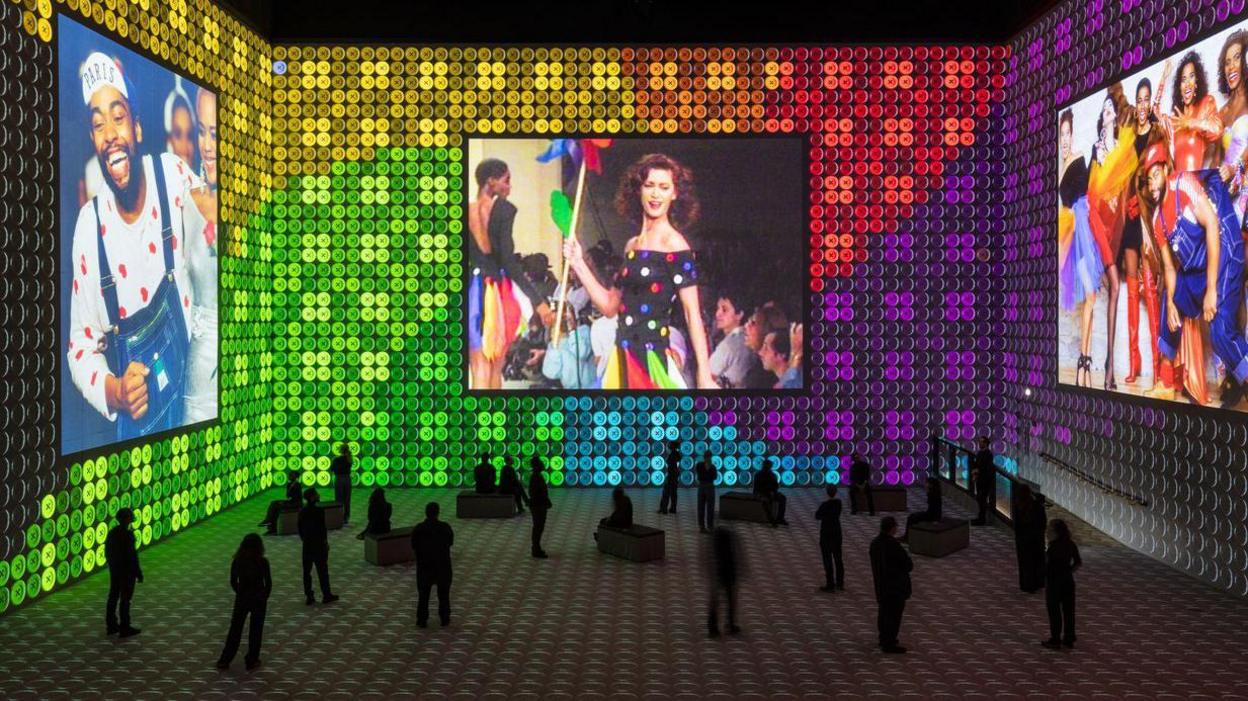 Fashion models are projected onto a multi panelled screen with green, sky blue and maroon backdrop