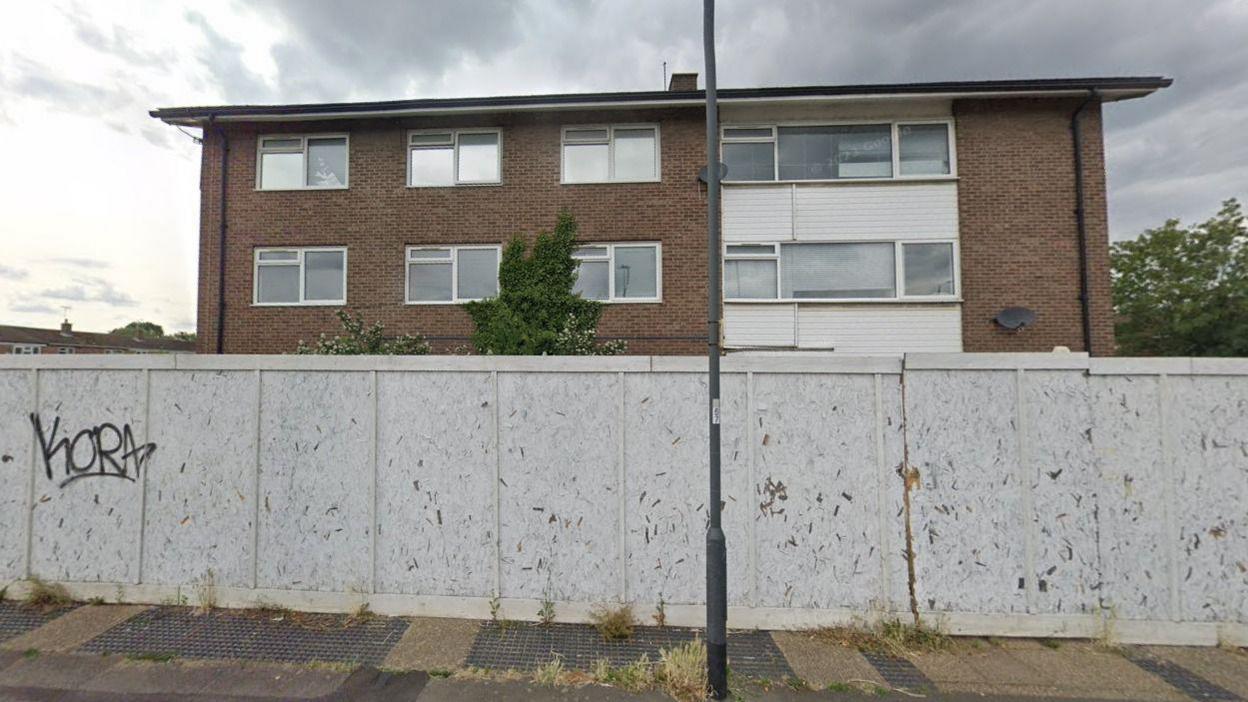 The site of former langley police station. It has white wooden boards in front, with a delapidated building behind it.