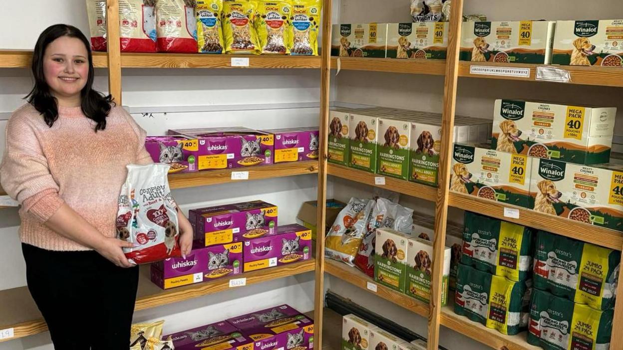 Tyesha Muncaster standing in a storage area surrounded by bags of dog and cat food