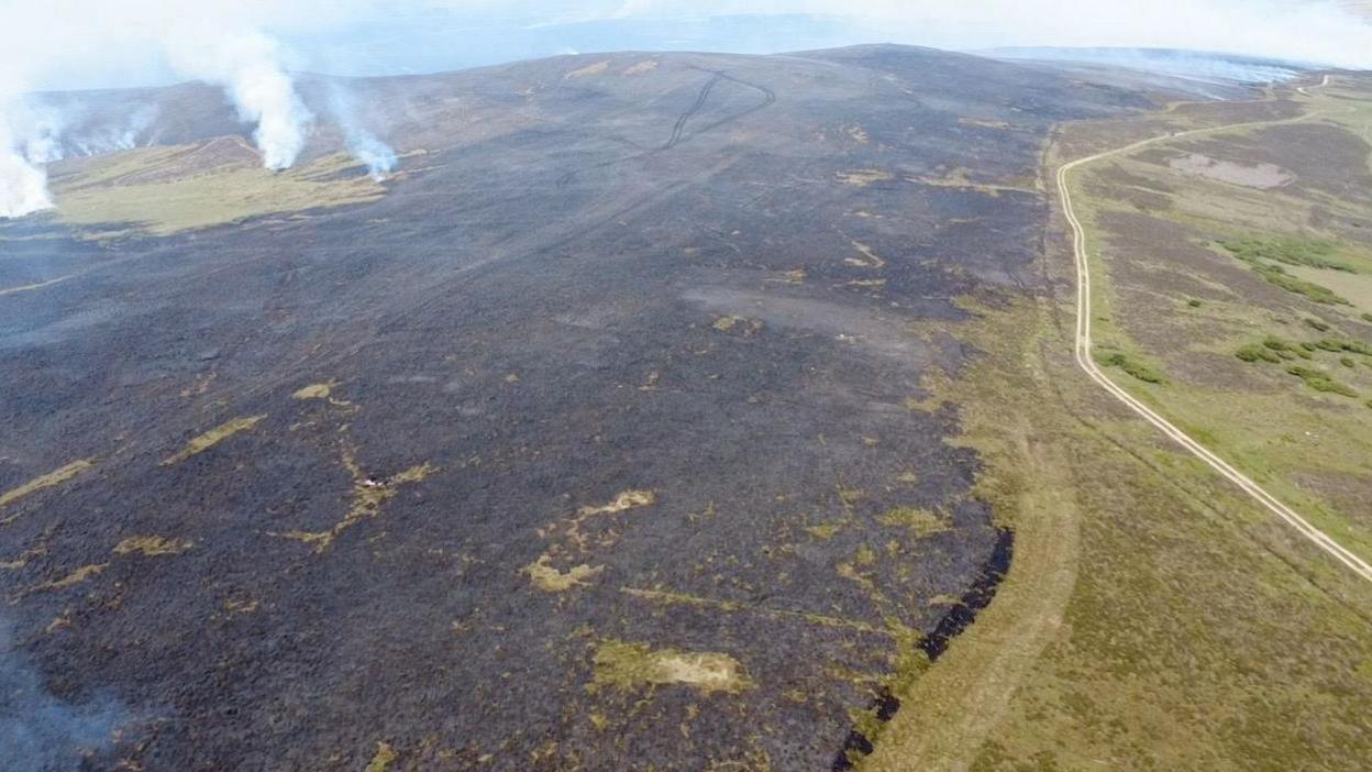 A drone image showing a large area of burnt moorland with fires still smouldering