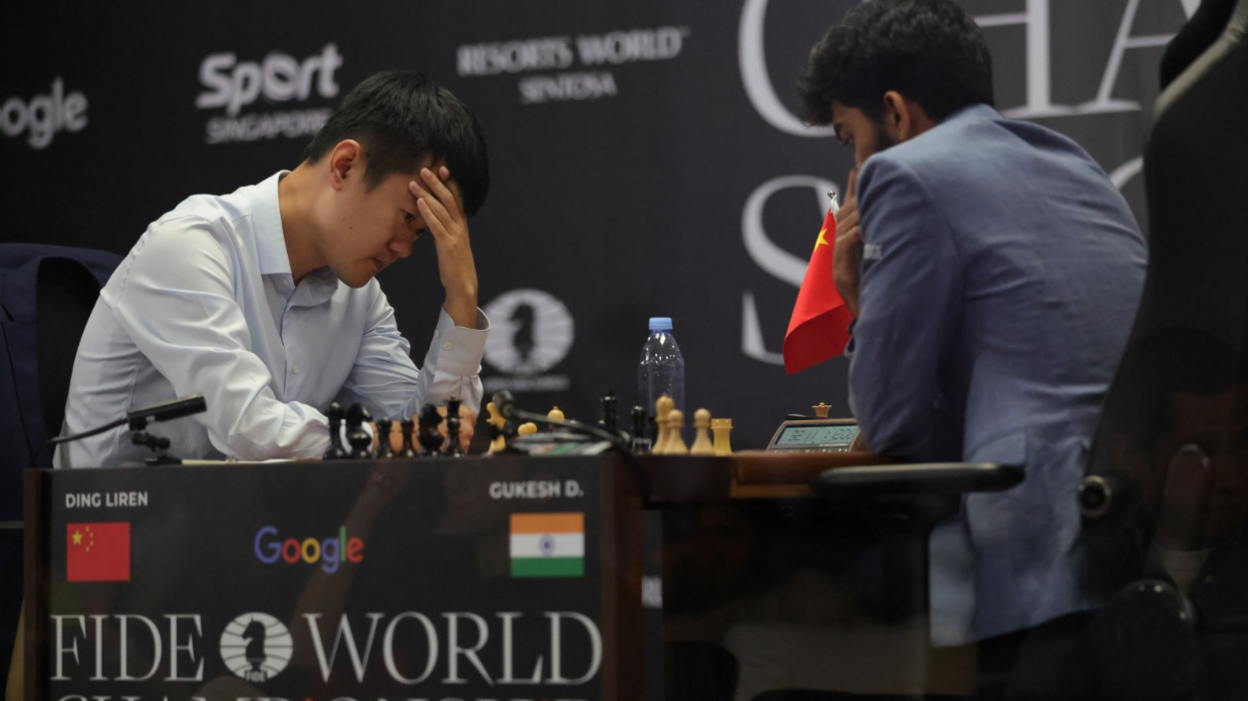 Ding Liren puts his head in his hands while playing opposite Gukesh Dommaraju. The two players are facing each other across the chess board