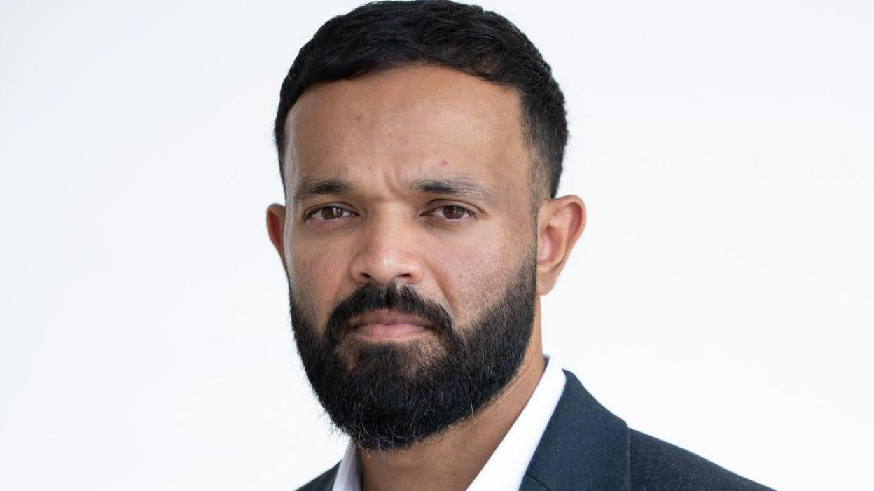 Azeem Rafiq, a bearded man wearing a white shirt and black blazer. The background is plain light.