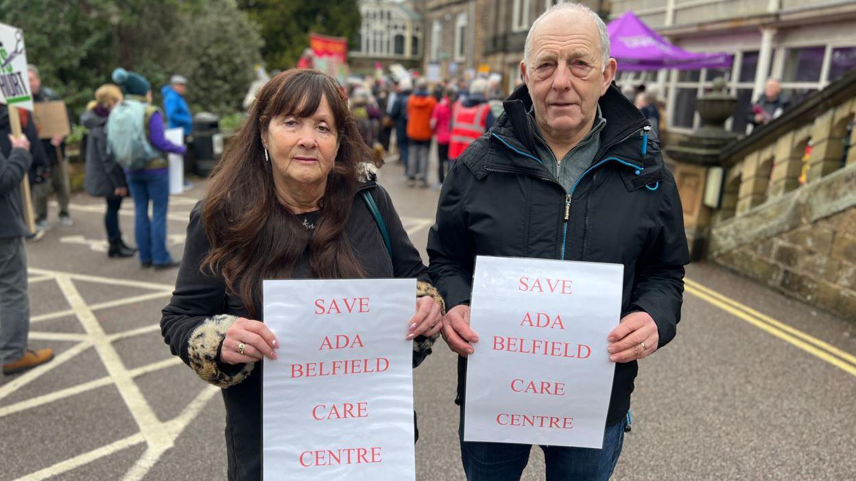 Pam Cox and her husband Paul outside the council HQ with signs that read "Save Ada Belfield Care Centre"