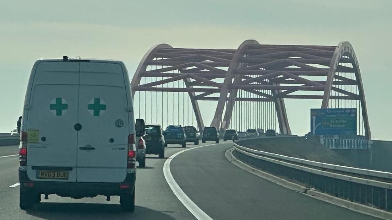 The convoy - a long line of vehicles in single file - travelling over a bridge. 