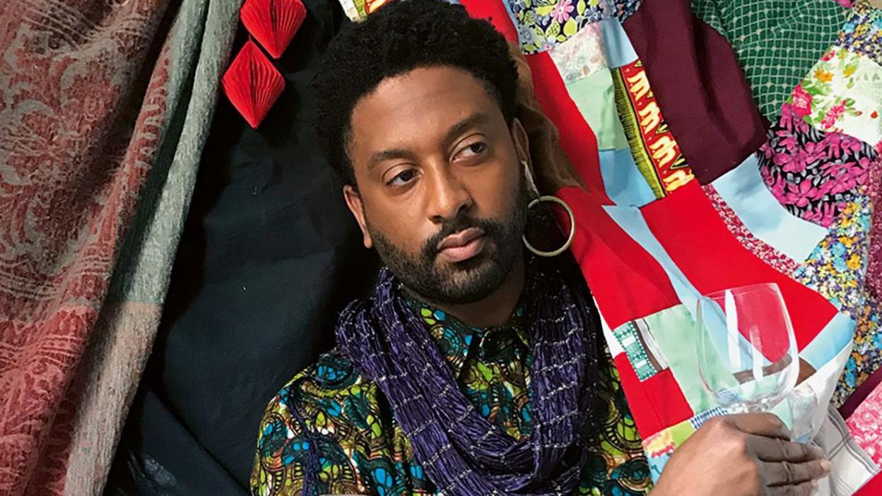 Peter Brathwaite recreating a historic picture, wearing colourful clothing and holding a wine glass