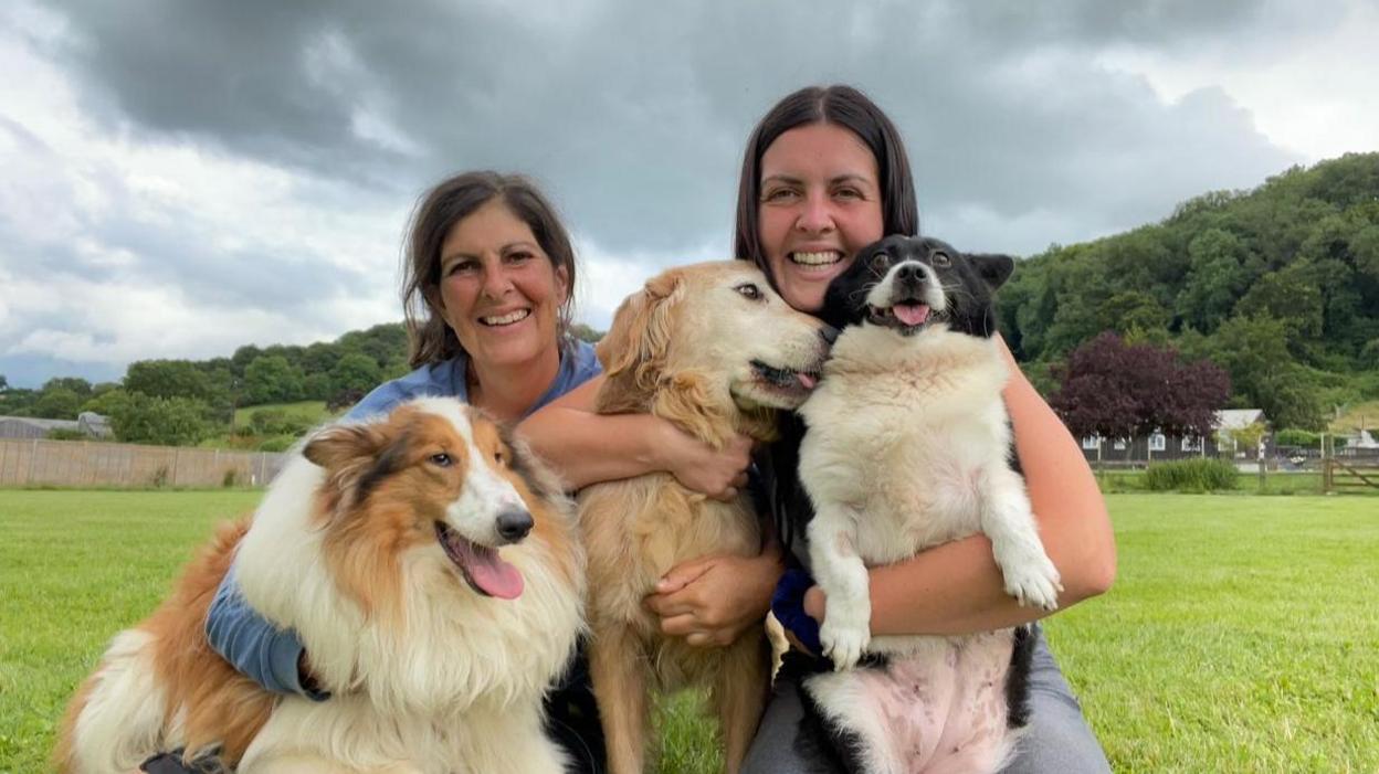 Two women cuddling dogs in a field.