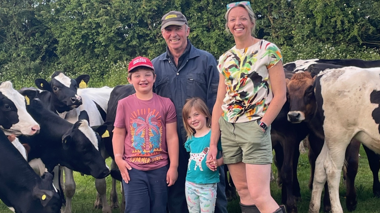 Robert and Lucy Noad with their young son and daughter surrounded by cows