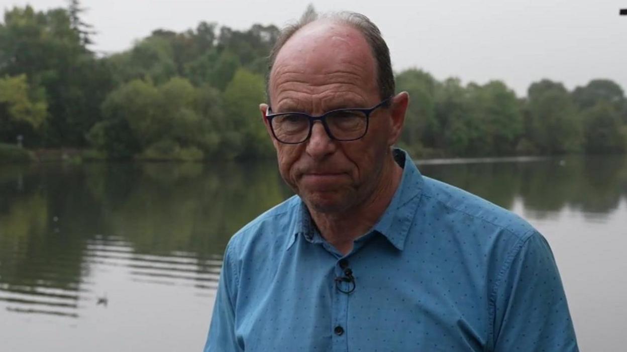 Ian McNuff standing pictured in front of the River Thames. He is wearing a blue shirt and glasses.