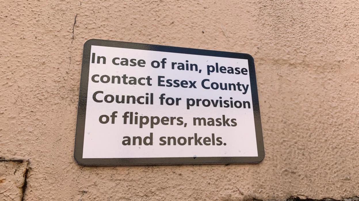 A close-up picture of sign above an underpass that reads: "In case of rain, please contact Essex County Council for provision of flippers, masks and snorkels."