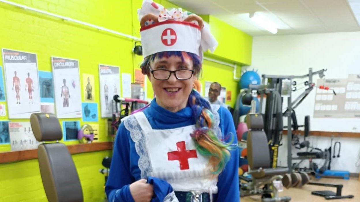 A woman in a fancy dress nurses outfit standing in front of weight machines in a gym.