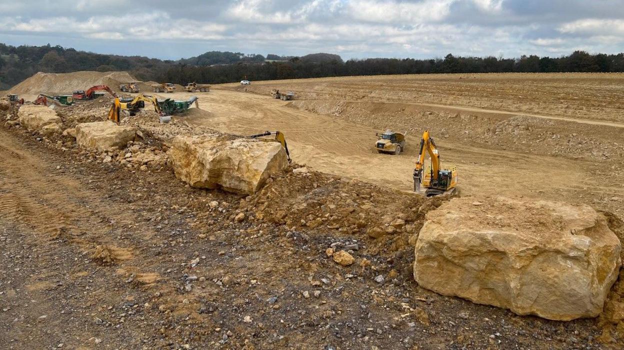 A view of the vast construction site with a few diggers dotted around a mass of brown earth and rocks