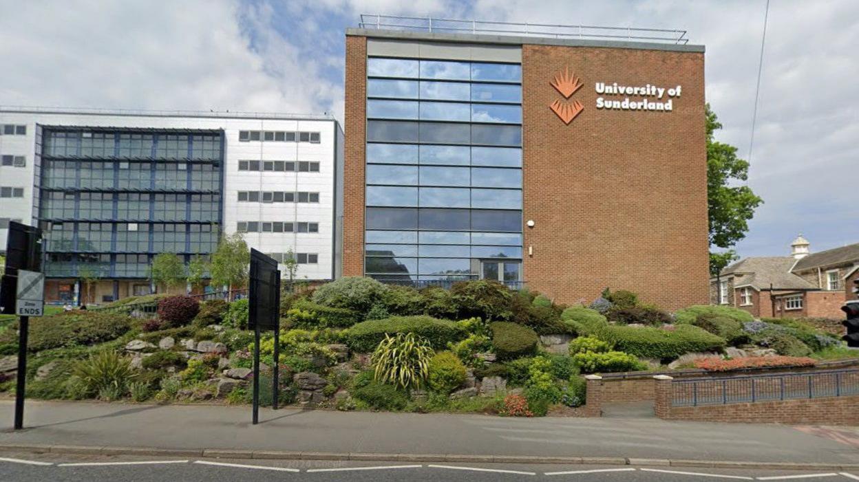 Brown brick building with windows reflecting blue sky. It has a large sign saying 'University of Sunderland' 