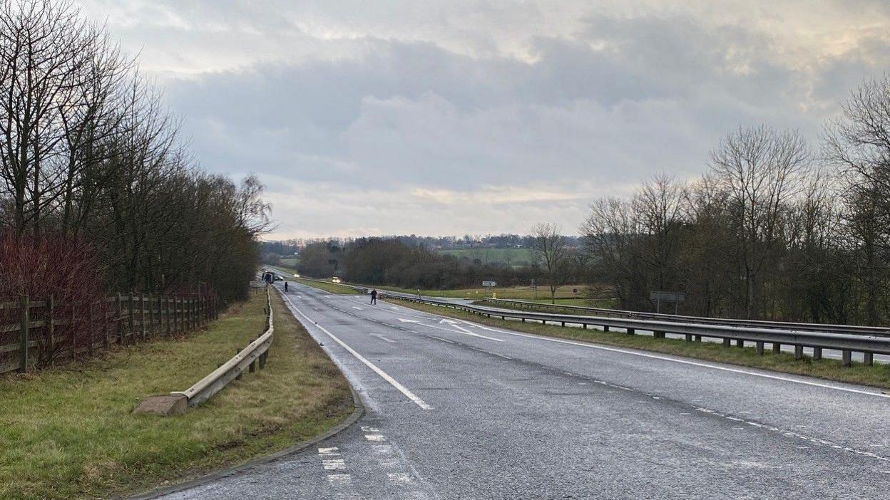 An empty A1 with a few emergency vehicles in the distance and two people in the road.