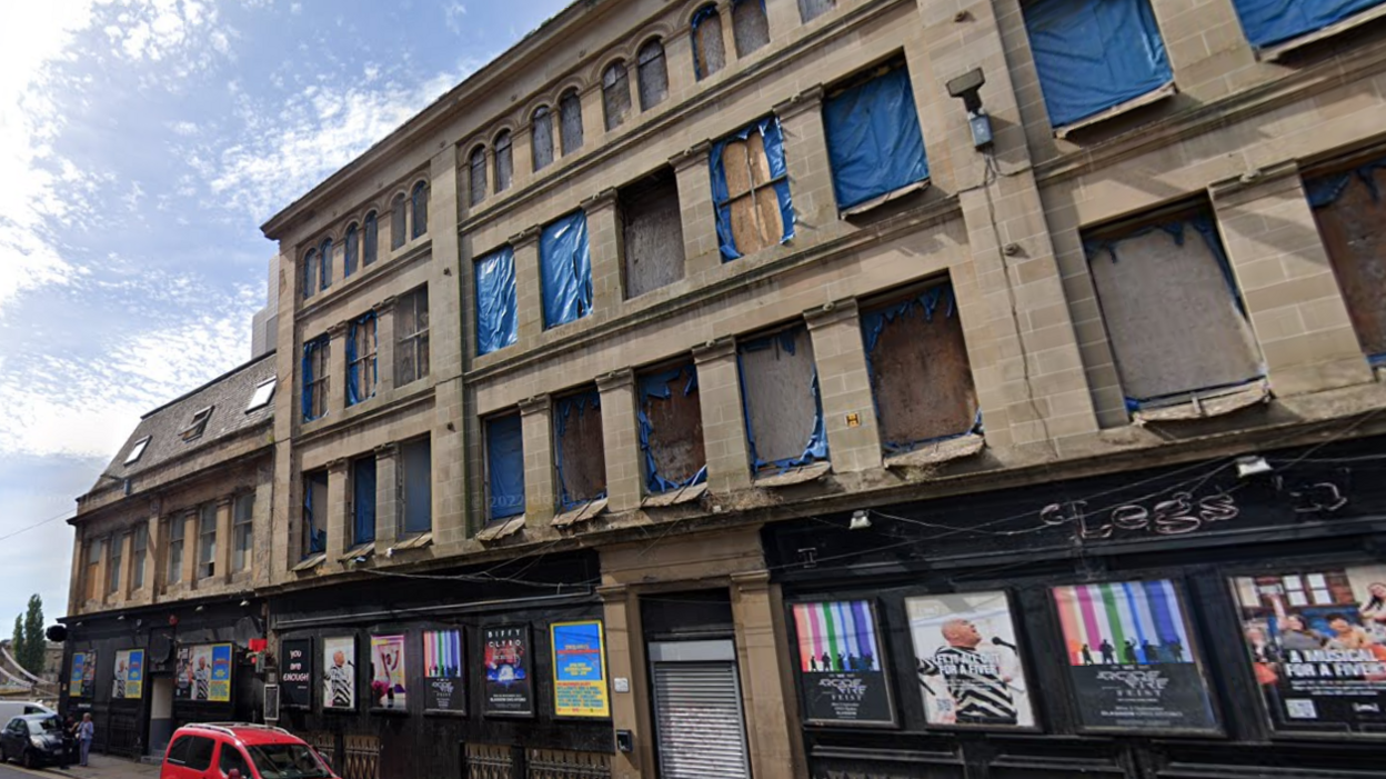 A derelict building on a street, with windows boarded up 