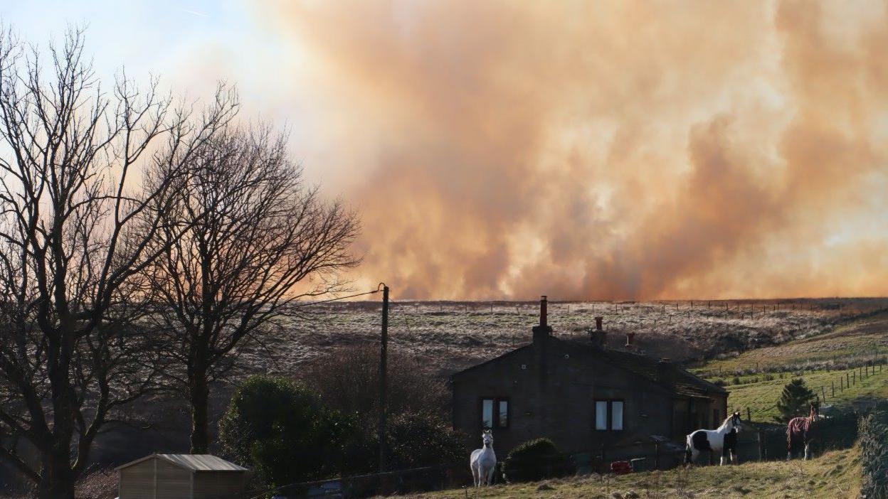 Smoke hovering on horizon near house on moorland