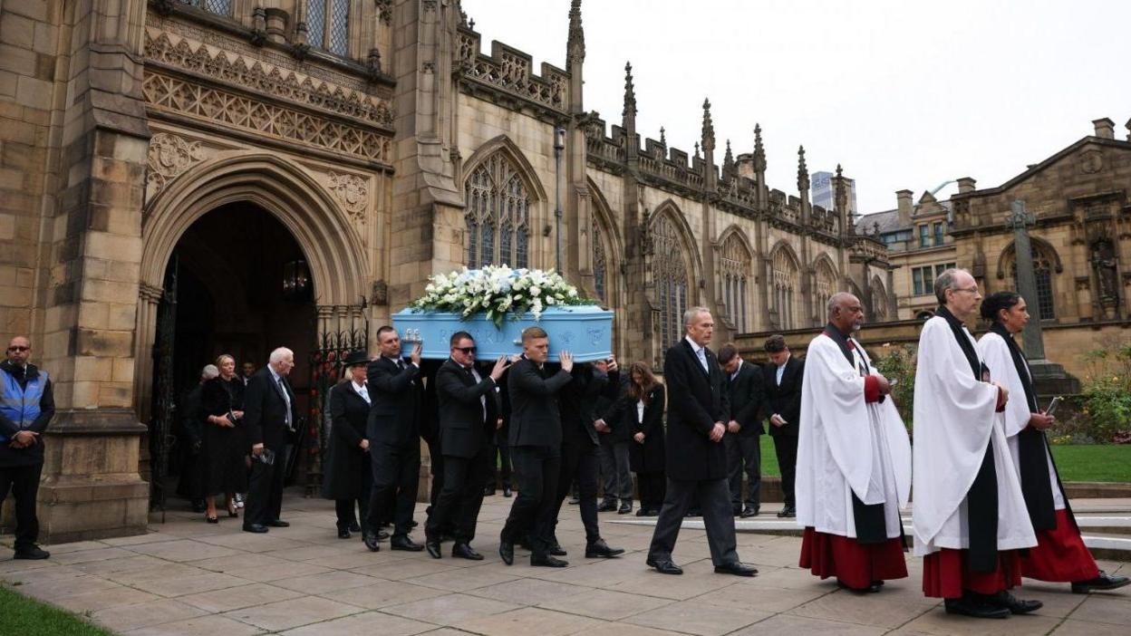 Pallbearers carry the coffin which is adorned with white flowers after the funeral service at Manchester Cathedral