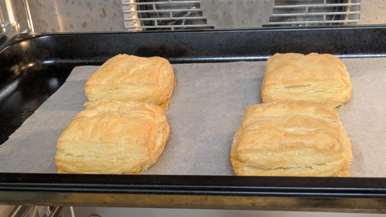 Hands holding a tray with cooked pastry on it. 