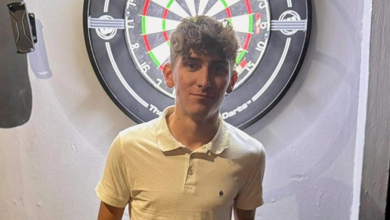 Tyler Thorpe poses in front of a dartboard