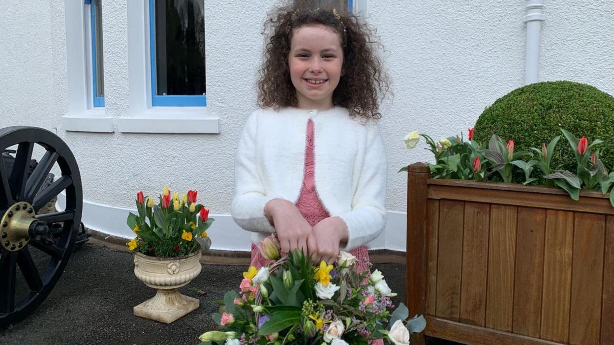 A young girl with curly hair smiling with flowers