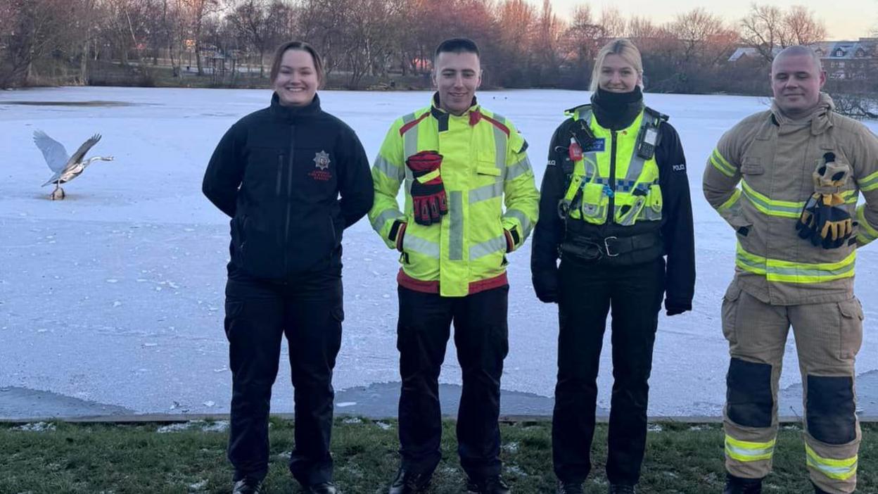 Police and firefighters, two male and two female, stand at the edge of a frozen pond with a large bird in flight pictured behind them