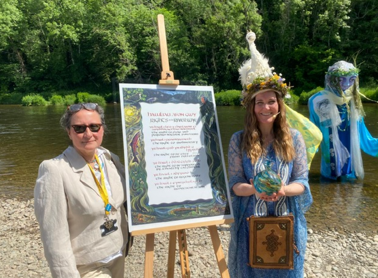 Two women stand either side of an easel on which the charter stands. One wears a linen suit, the other wears a long blue gown