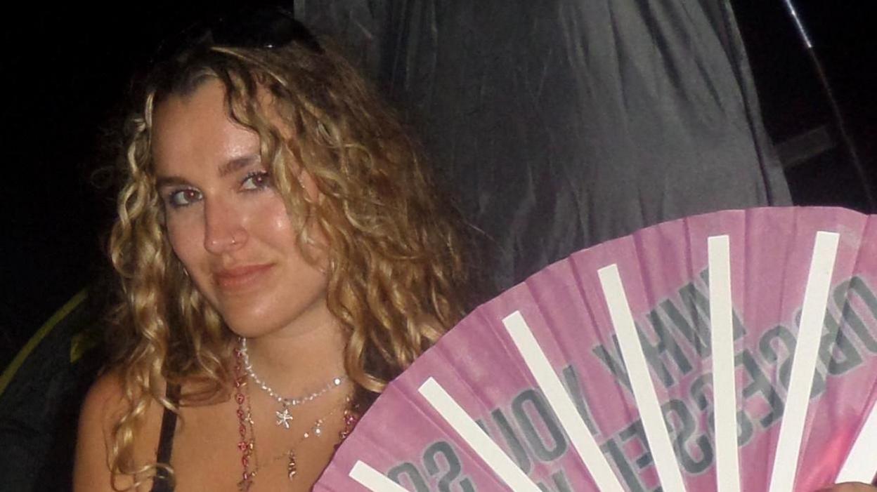 A woman with blonde wavy hair stares at the camera. 