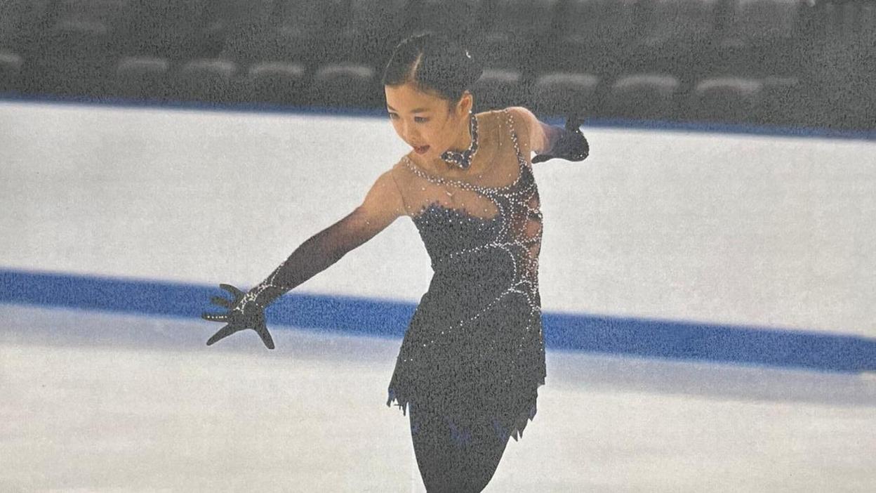 Jinna Han, a young woman with black hair, skates in an ice rink wearing a black costume.