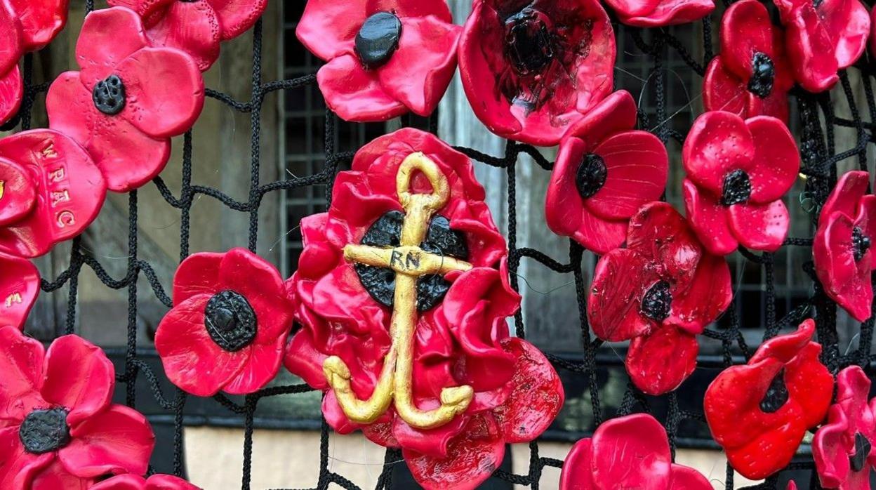 Dozens of ceramic poppies attached to netting in front of windows.