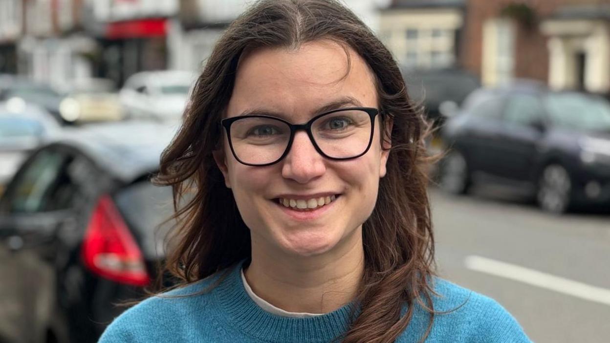 Leah in Eccleshall High Street. She wears glasses and a blue jumper. 