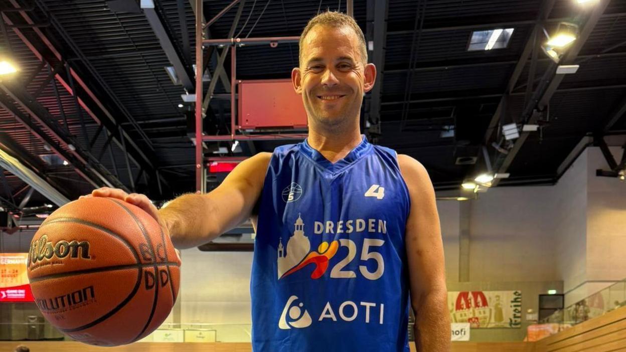 A man smiling holding a basketball courtside